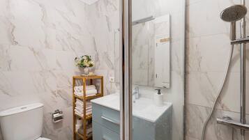 A bathroom with a toilet, a sink, a shower, and a glass-enclosed shower area.