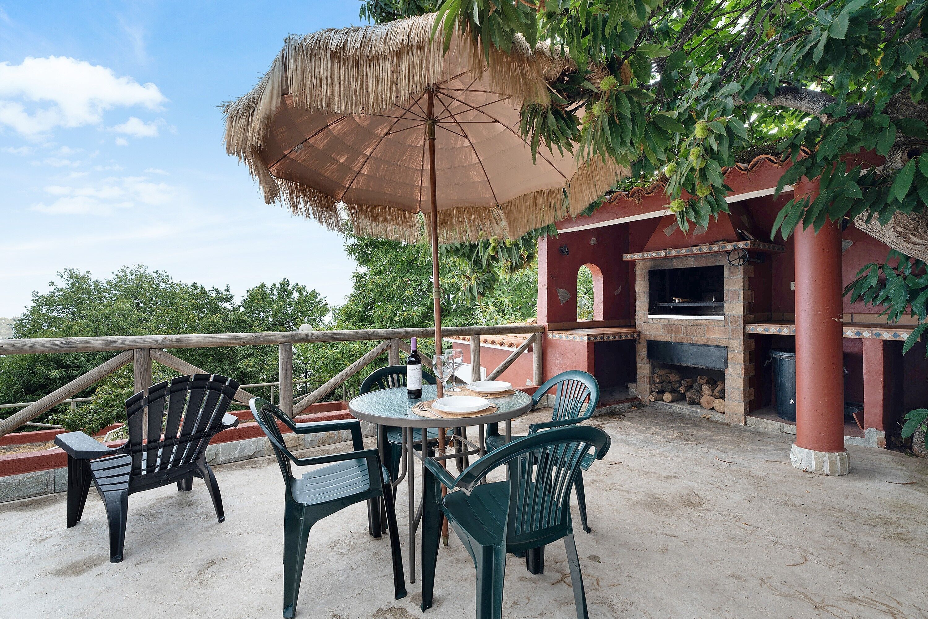 An outdoor patio with a round table, chairs, a thatched umbrella, and a grill.
