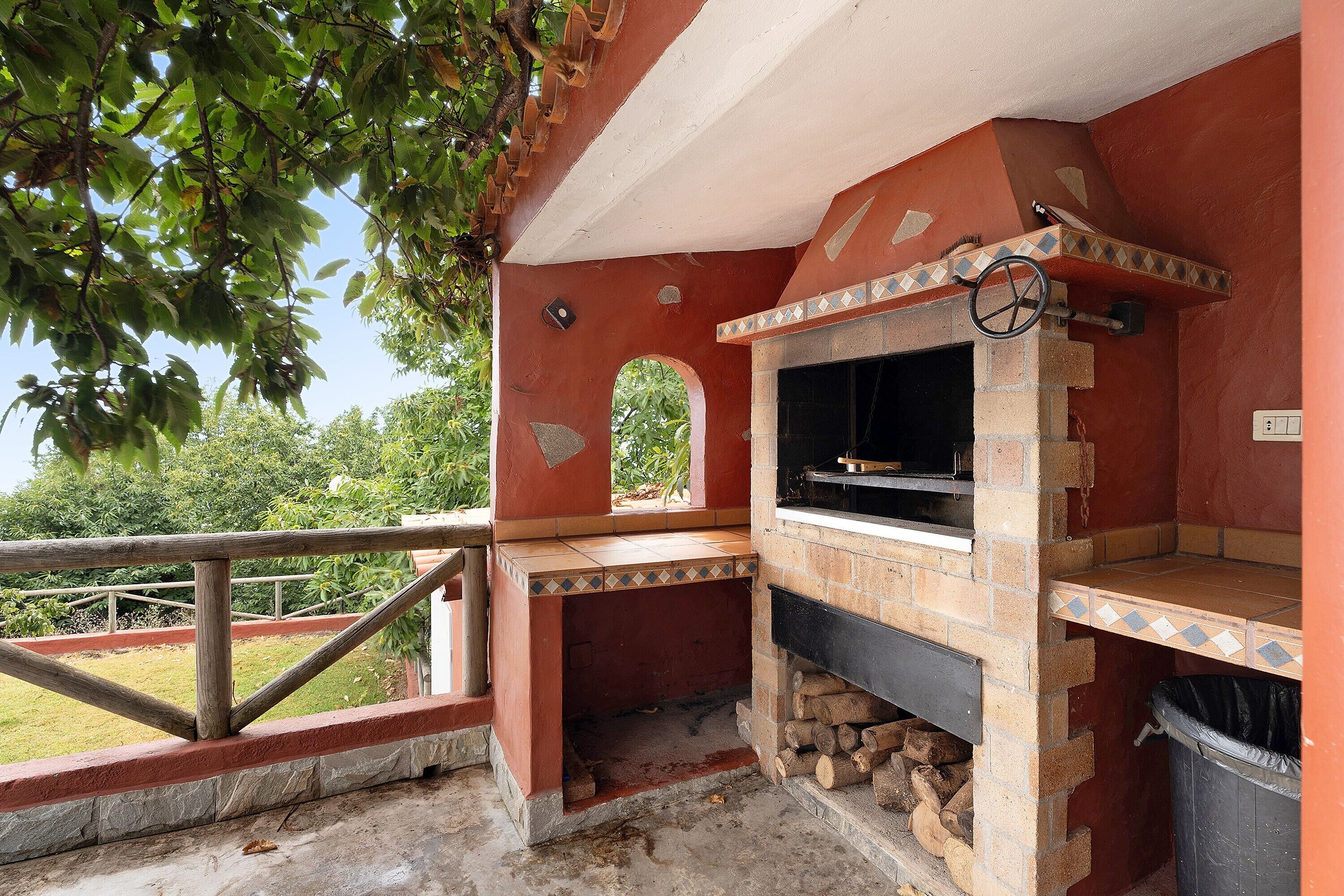 A brick-built outdoor kitchen with a chimney, a trash bin, and a wooden railing.