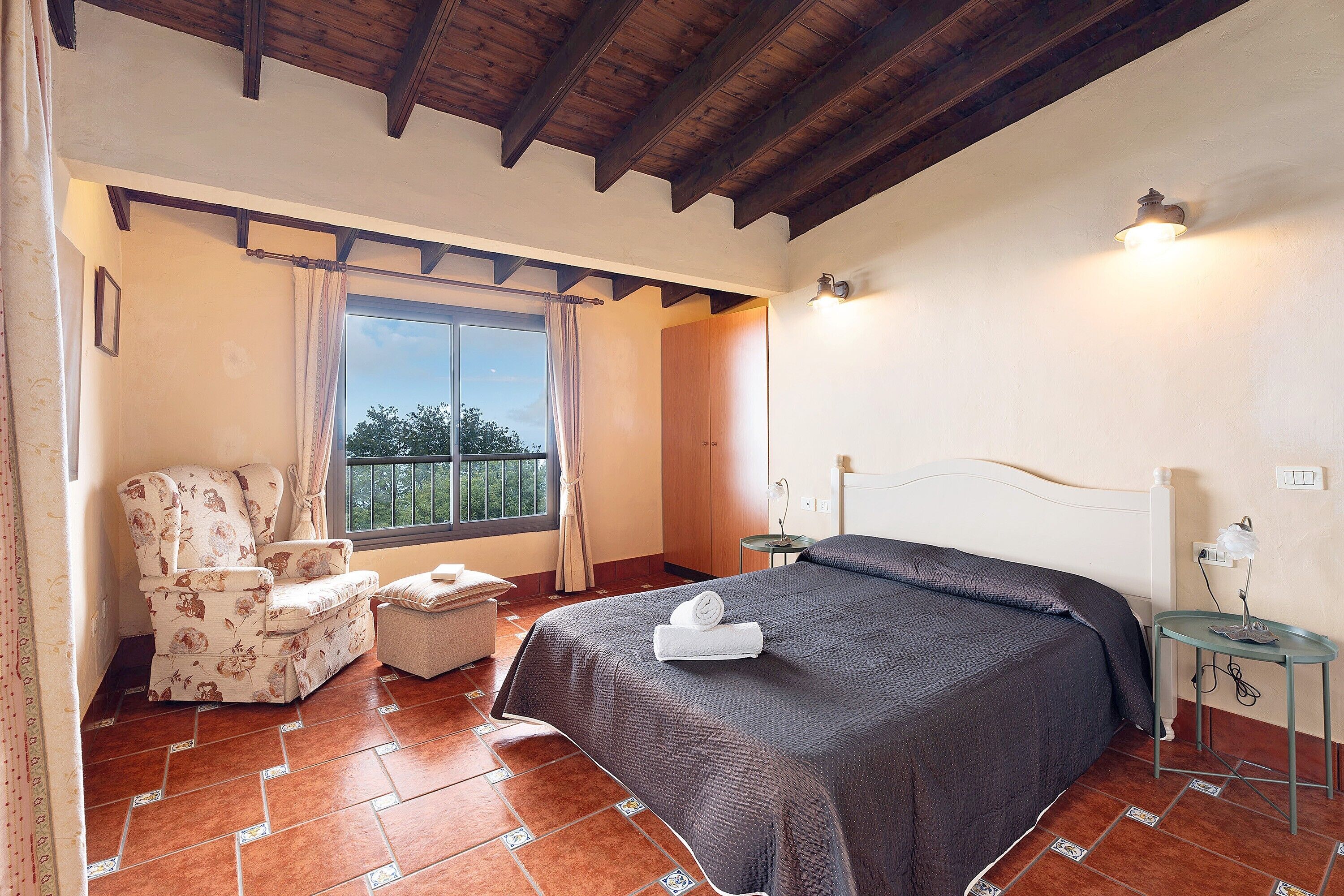 A bedroom with a bed, a chair, a window, and a balcony.
