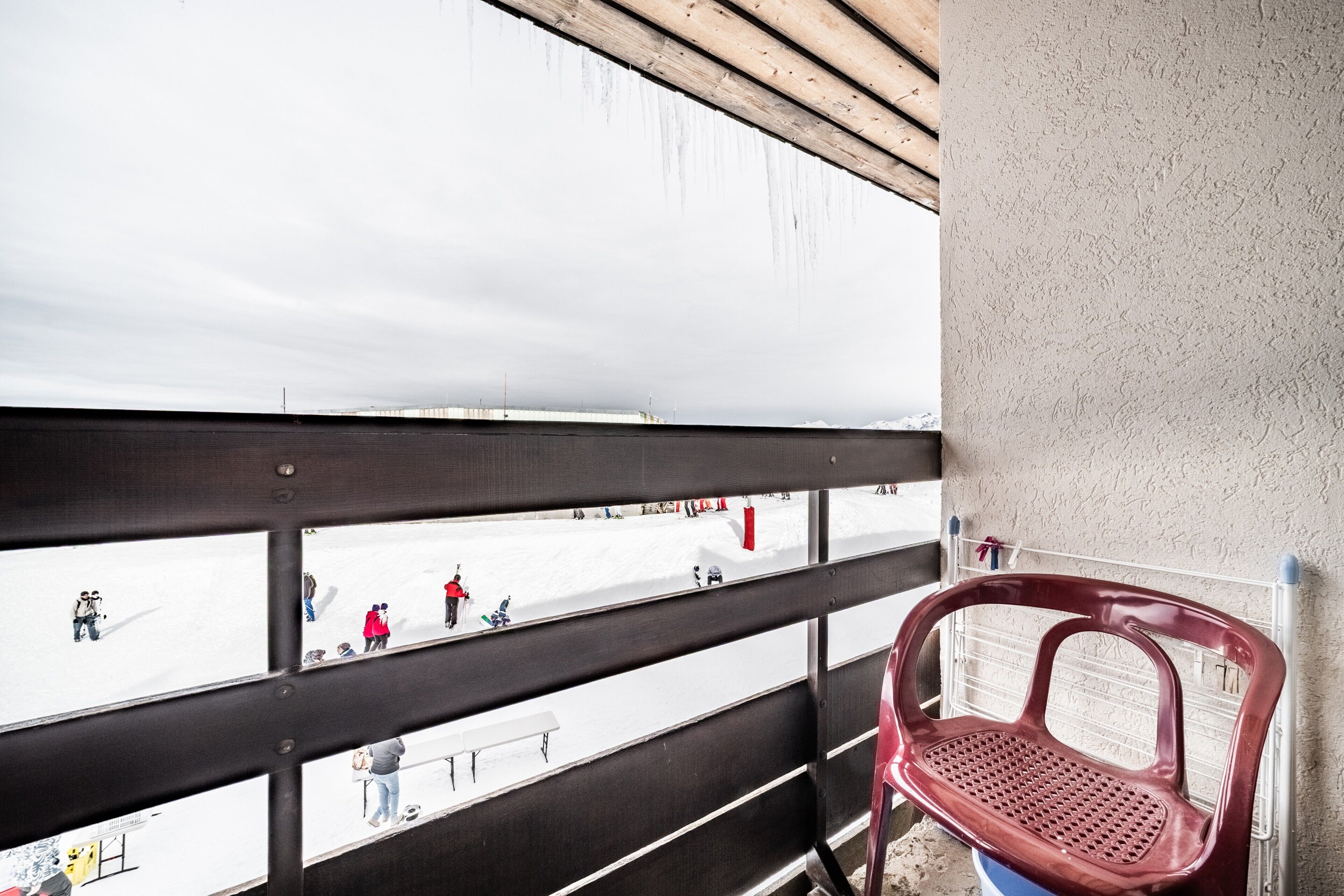 A balcony with a view of a snowy landscape, a red plastic chair, and a metal railing.