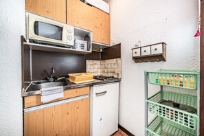 Une cuisine de taille réduite équipée d’un four à micro-ondes, d’une cuisinière, d’un évier et d’armoires en bois.