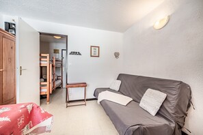 Un espace de vie compact comprenant un canapé, une petite table, une armoire et une porte donnant sur un placard.