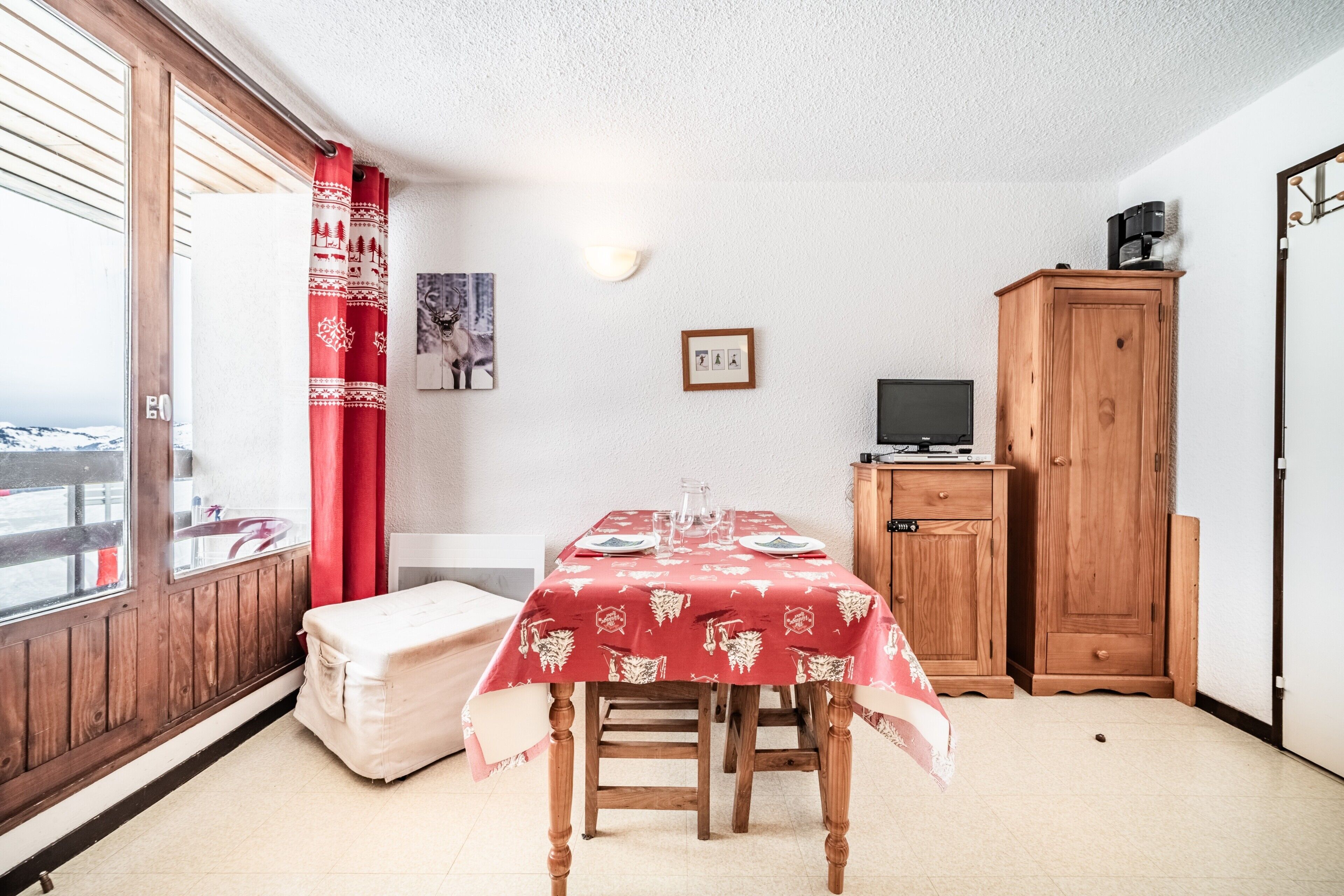 A room with a dining table, a sofa, a wooden cabinet, and a television.