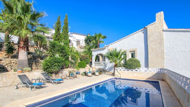 Una piscina con sillas de descanso, palmeras y un edificio blanco de fachada de piedra.
