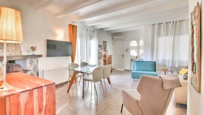 Una sala de estar moderna con una mesa de comedor de vidrio, dos sillas, un sofá y un televisor montado en la pared.