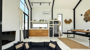 A modern living room with a black sectional sofa, a wooden coffee table, and a kitchen area with a built-in fridge and microwave.