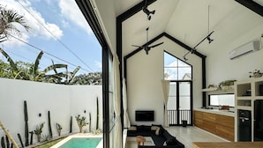 A modern living space with a pool, ceiling fans, and a kitchen area.
