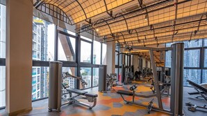 Academia com diversos equipamentos de exercício, janelas amplas e pé direito alto.