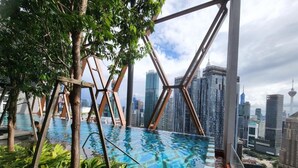 Una piscina infinita a la terrassa amb vista a l'horitzó urbà, envoltada de vegetació i estructures metàl·liques.