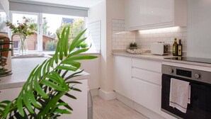 A modern kitchen with white cabinets, a built-in oven, and a window with a view of the outside. - Stunning Townhouse with Large Garden - Sleeps 8 (Cheltenham)