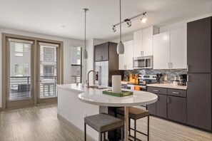 A modern kitchen with a central island, stainless steel appliances, and a large window with blinds. - TWO Modern Waterfront Cozysuites sidebyside (Tempe)