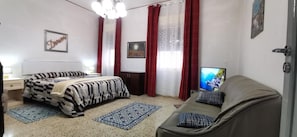 Un dormitorio con cama, sofá, televisor, escritorio y silla.