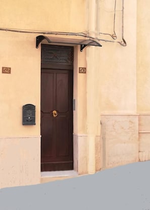 Una puerta marrón con picaporte de latón, flanqueada por dos buzones, con el número '52' a la izquierda y '50' a la derecha.