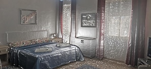 Un dormitorio con cama, mesita de noche, lámpara, televisor y puerta con pared texturizada.