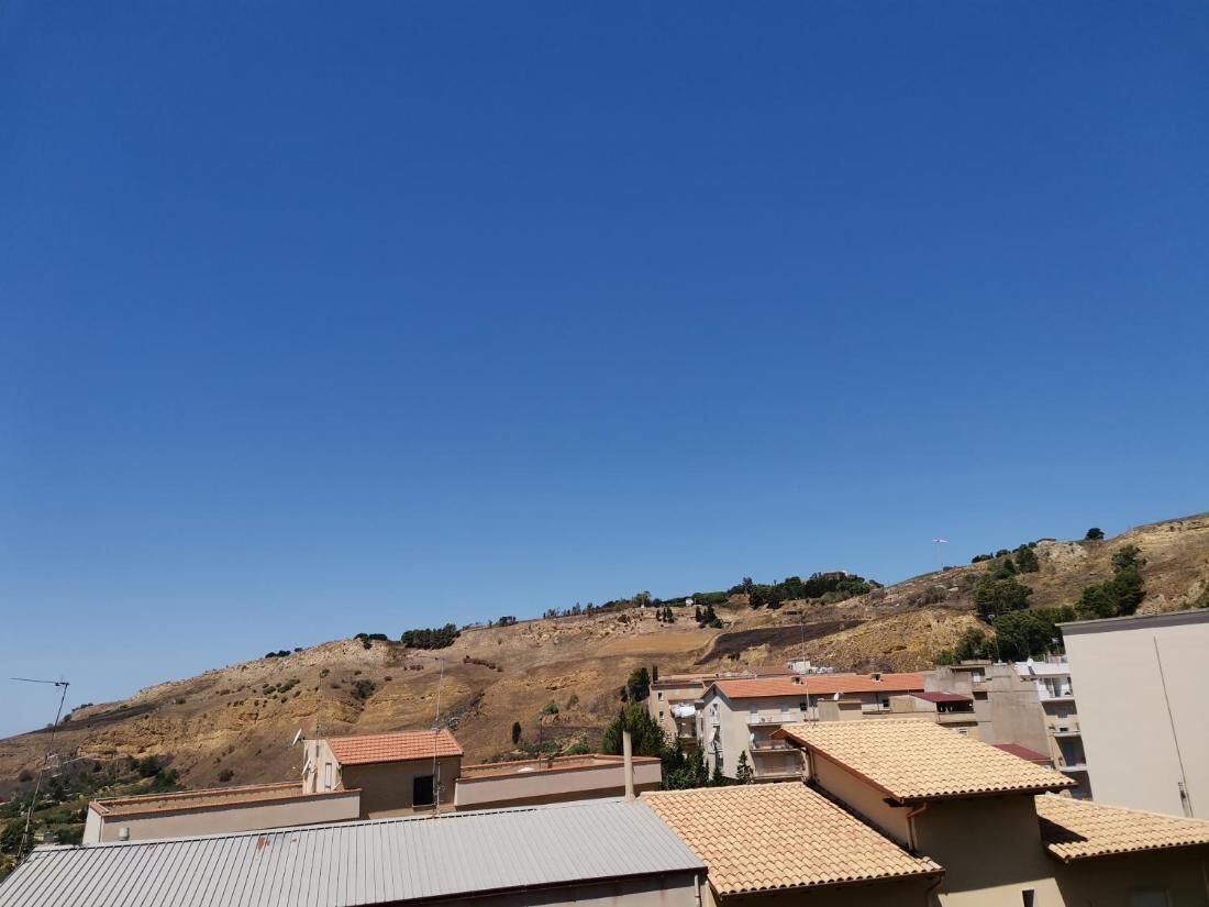 A residential area with buildings on a hillside, clear sky, and a distant view of a hill.