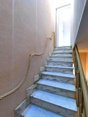 Una escalera de mármol con una barandilla de cuerda, que lleva a una puerta en la parte superior.