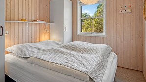 Een slaapkamer met een bed, een kledingkast, een raam met uitzicht op bomen en een hangende lamp.