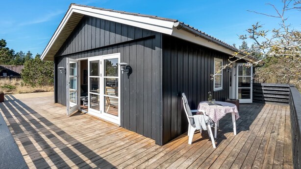 Een klein, donker houten vakantiehuisje met een terras, een tafel en stoelen.