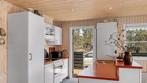 Een moderne keuken met witte kastjes, een rood aanrecht en uitzicht op de omgeving door een glazen deur.