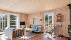 Een gezellige woonkamer met een bank, fauteuil en een klein tafeltje. Er is een open haard en een televisie die aan de muur is bevestigd.