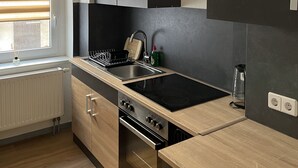 A modern kitchen with a built-in stove, oven, and sink, wooden cabinets, and a pendant light. - Comfortable vacation apartment with contactless check-in and digital guest directory (Pasewalk)