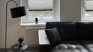 A modern living room with a black leather sofa, a floor lamp, and a radiator. - Comfortable vacation apartment with contactless check-in and digital guest directory (Pasewalk)