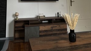 A modern living room with a flat-screen TV mounted on the wall, a wooden entertainment unit below, and a door to the right. - Comfortable vacation apartment with contactless check-in and digital guest directory (Pasewalk)