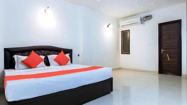 Una habitación de hotel moderna con una cama grande, dos almohadas rojas, ropa de cama blanca y un cabecero negro.