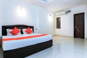 A modern hotel room with a large bed, two red pillows, white bedding, and a black headboard. - Hotel Krishna Cottage - Vrindavan (Mathura)