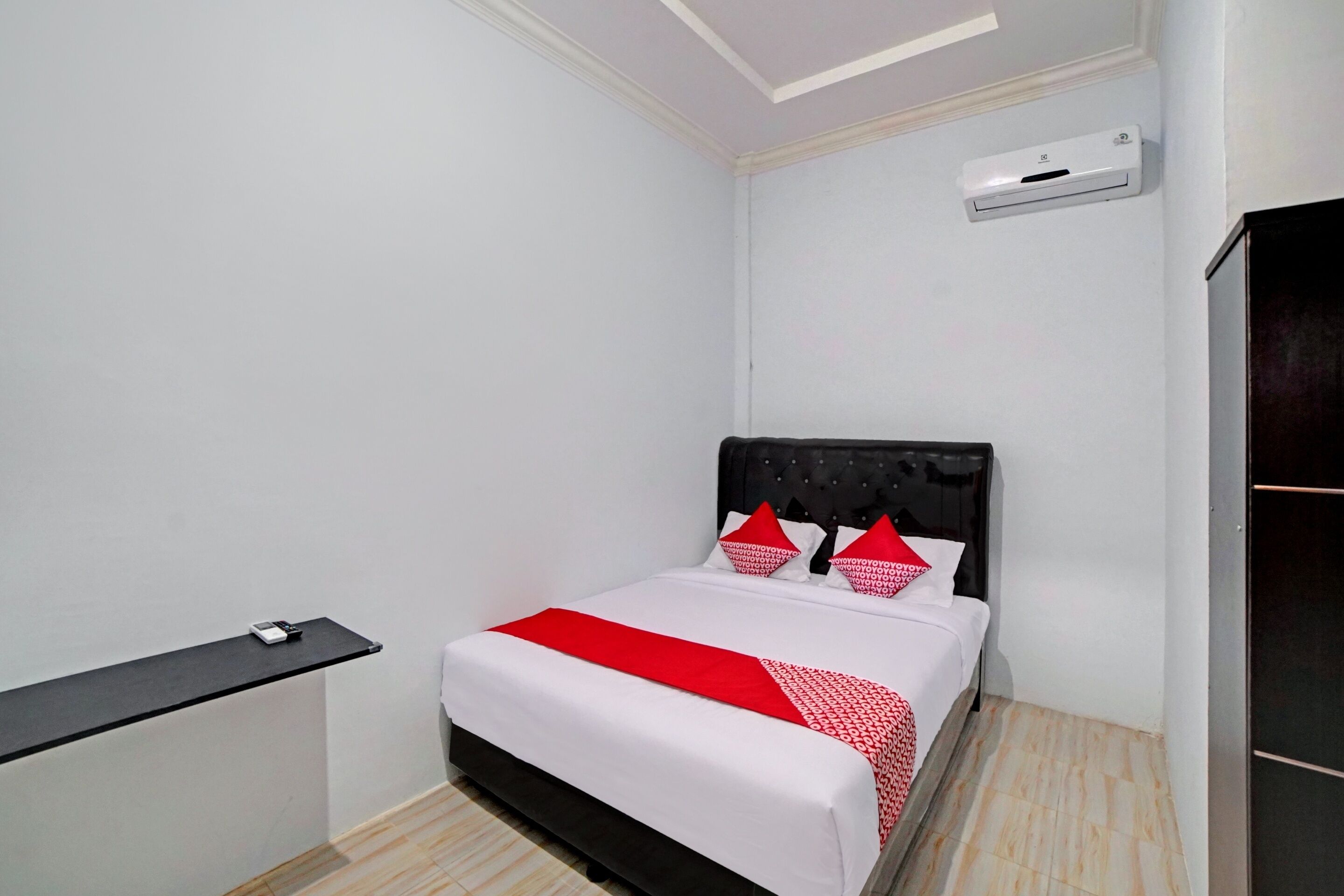 Een compacte, verzorgde slaapkamer met een bed, nachtkastje, een wandairconditioner en een donkergrijze garderobe.