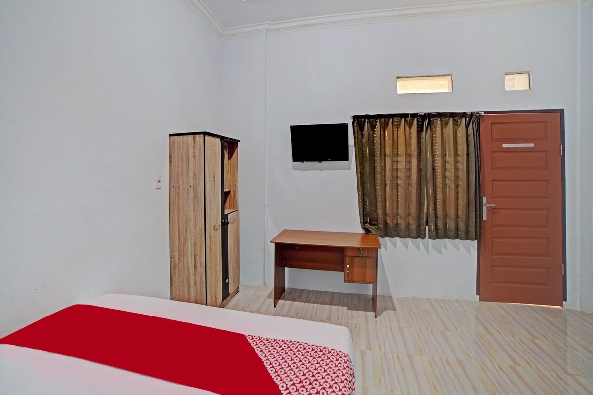 Habitación de hotel con cama, escritorio, armario, televisor y puerta.