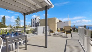 Un patio techado al aire libre con una mesa, sillas, una pizarra y vista al océano.