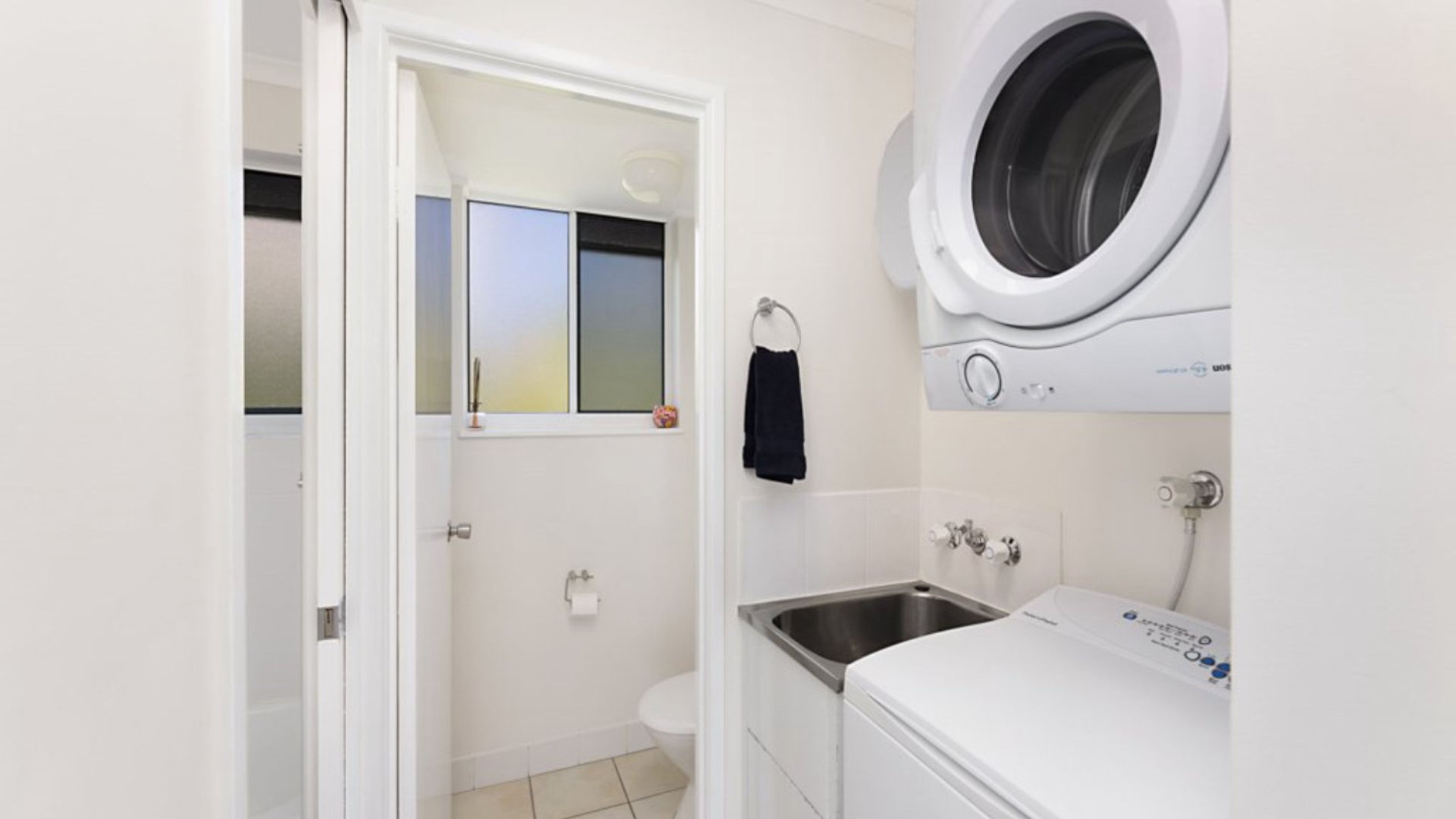 Une petite buanderie équipée d’un lave-linge, d’un évier et de toilettes.