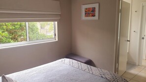 A bedroom with a bed, a window, a door, and a framed picture on the wall.