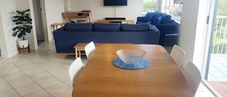 A modern living room with a wooden dining table, blue sofa, and a flat-screen TV mounted on the wall.