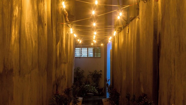 A narrow corridor with string lights, concrete walls, and a wet floor. - ALONA BEACH SIDE INN (Panglao)