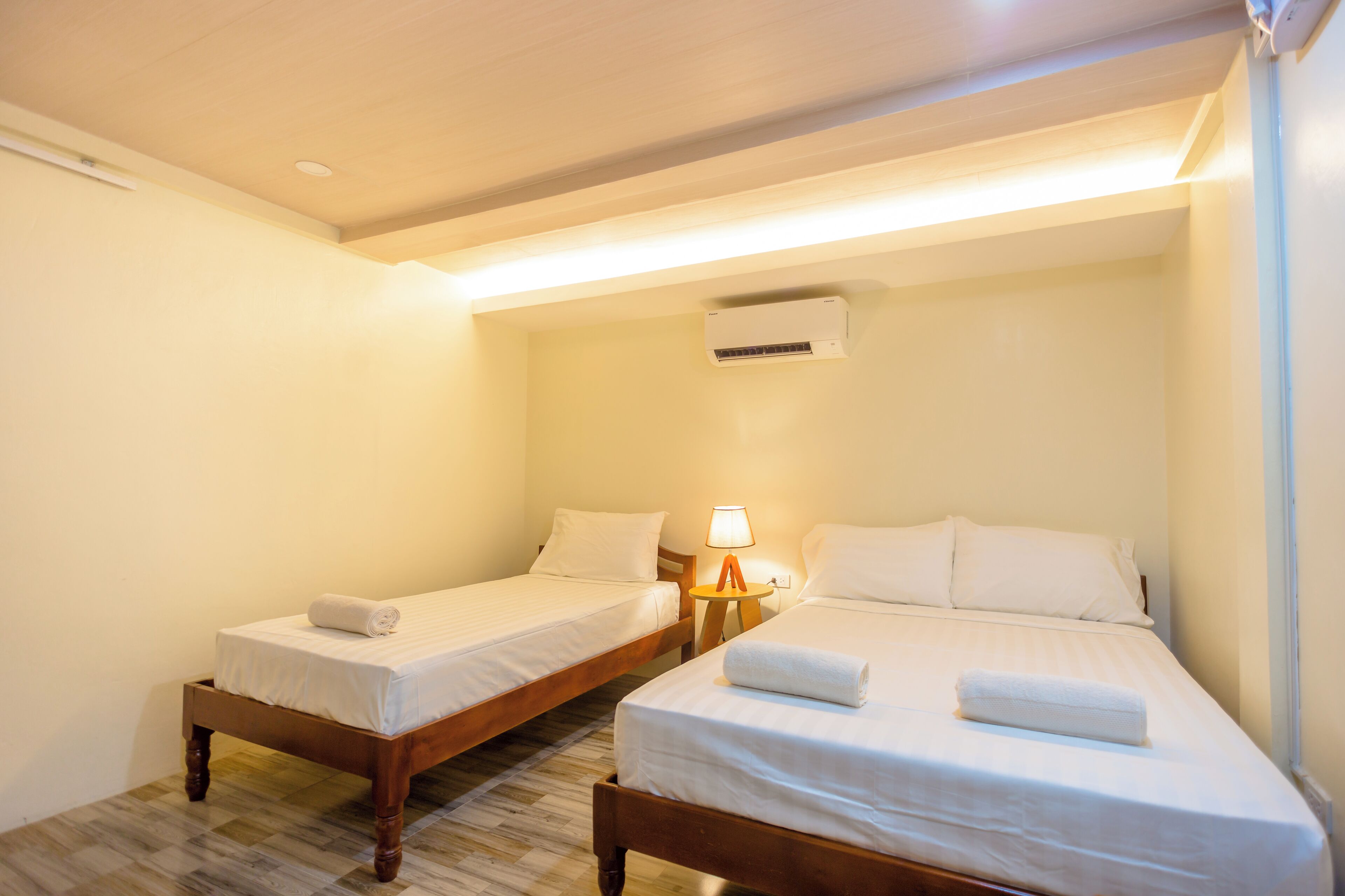 A room with two single beds, a nightstand with a lamp, and an air conditioning unit on the wall.
