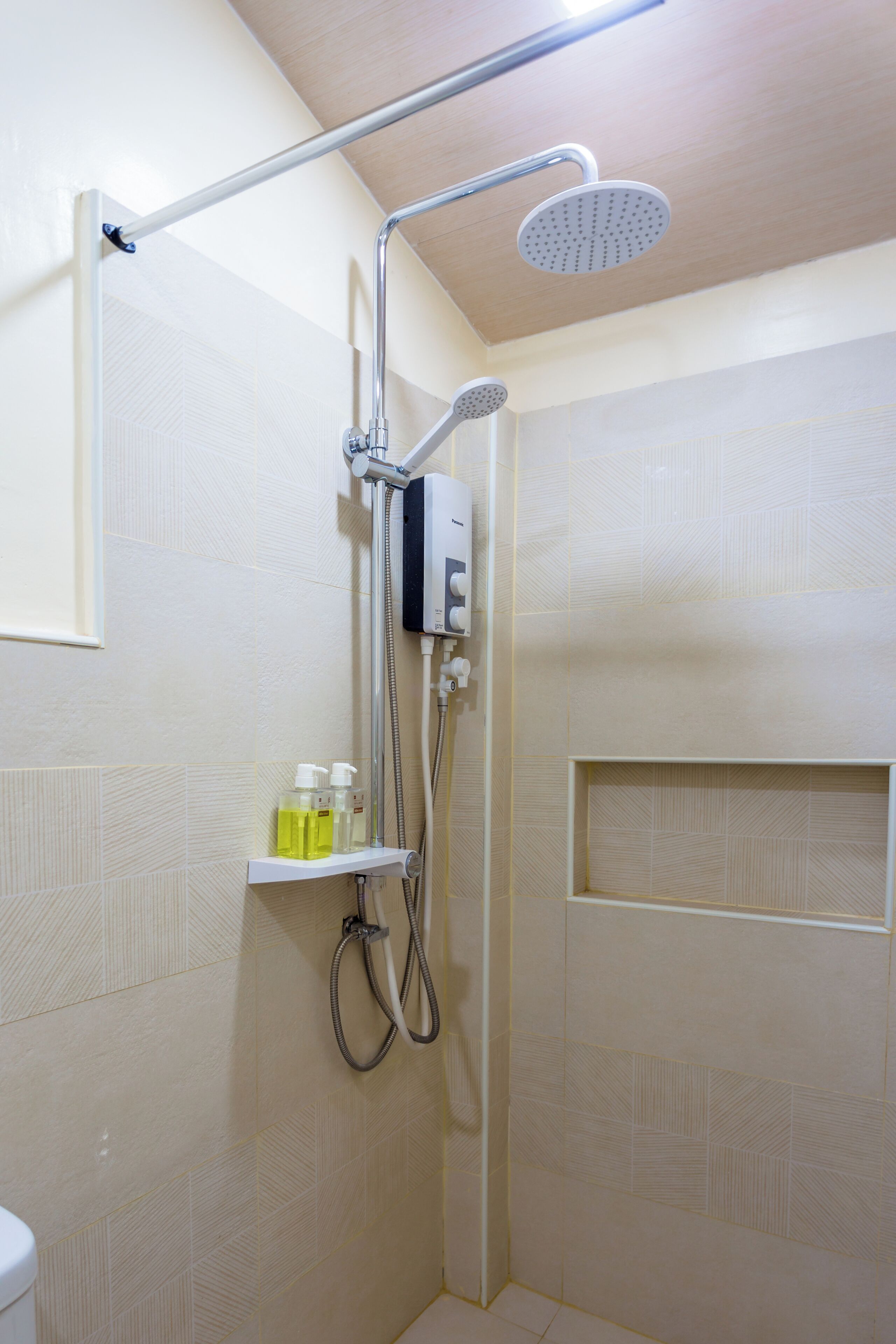 Zona de ducha con cabezal de ducha manual, panel de control en la pared y estante con artículos de aseo.