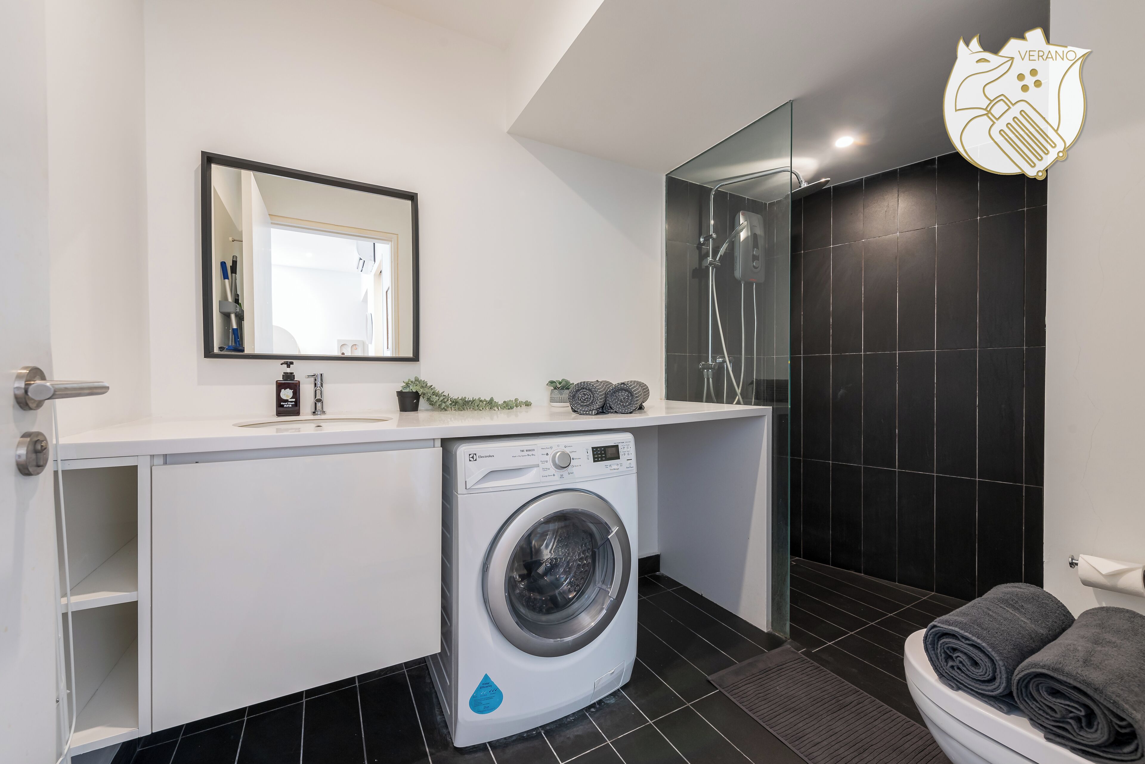 A modern bathroom with a washing machine, a mirror, and a shower area.
