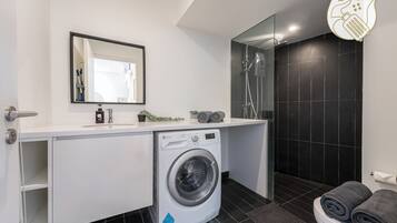 A modern bathroom with a washing machine, a mirror, and a shower area.