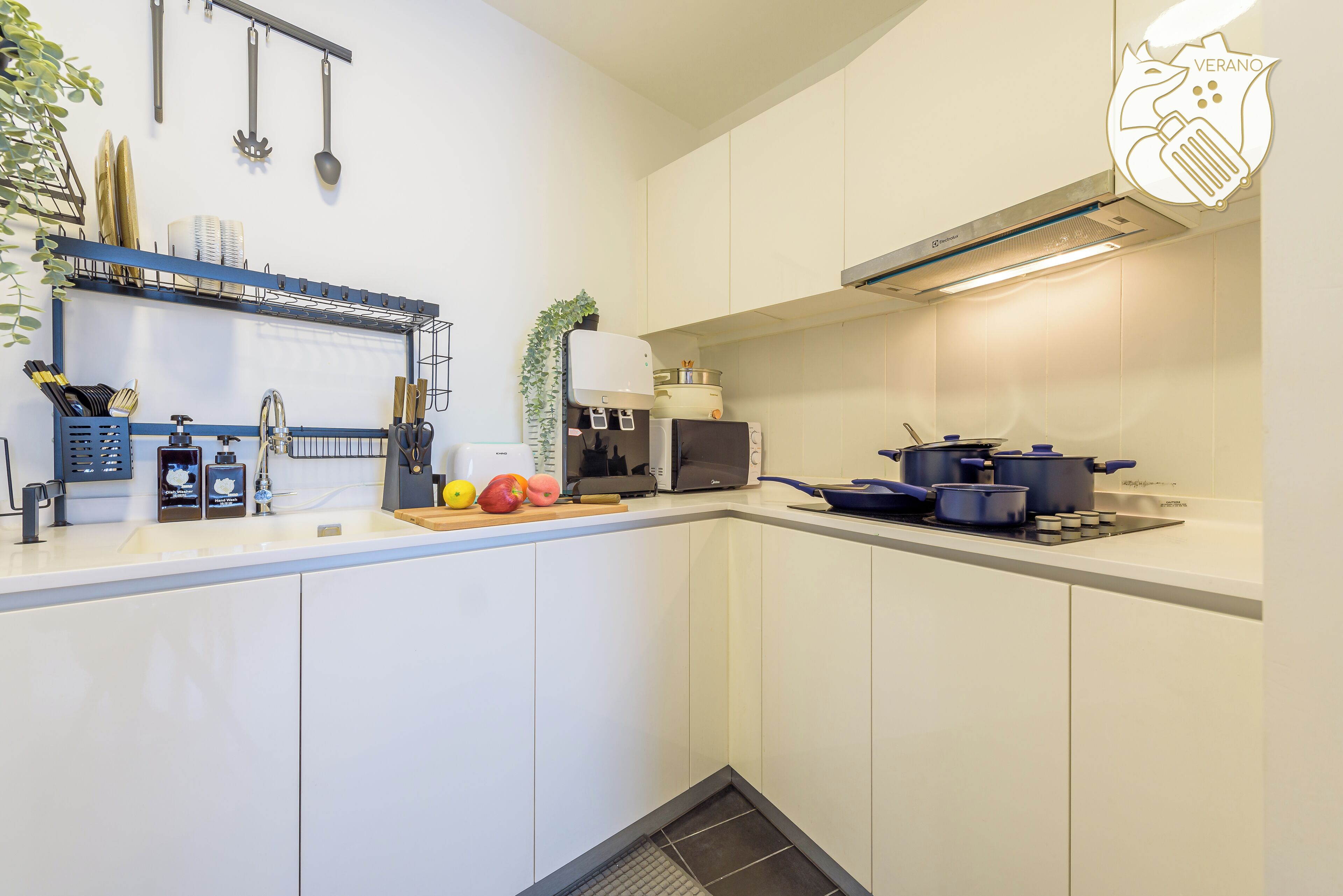 Une cuisine moderne avec des armoires blanches, un four encastré, un four à micro-ondes et une cuisinière. On peut voir des fruits sur le comptoir, et une plante est également visible.