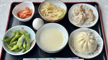 A tray with various food items including edamame, a bowl of soup, dumplings, and a plate of steamed buns.