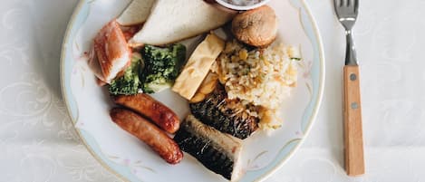 Un plato con diversos alimentos, como salchichas, pan y arroz, acompañado de una taza de té y un tenedor sobre una mesa con mantel estampado.