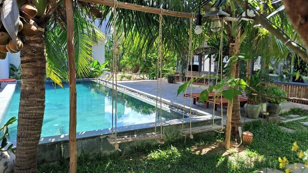 Una piscina rodeada de exuberante follaje, terraza de madera y mobiliario exterior.