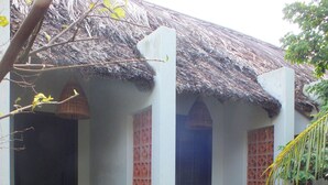 Una casa tradicional con techo de paja, un pequeño porche y un jardín con plantas y un estanque.