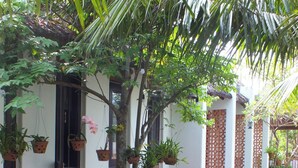 Un espacio al aire libre techado con una terraza de madera, plantas en macetas y un camino de piedra.