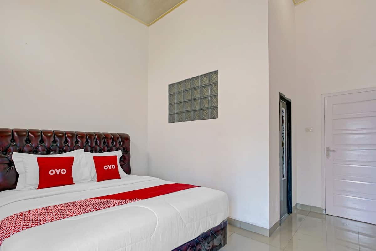 A neatly made bed with a red and white bedspread and two pillows with "OYO" branding.