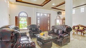 A luxurious living room with dark leather sofas, a glass coffee table, and a large wooden door with intricate designs. - OYO 90585 Saka Ganta Guest House Syariah (Terbanggi Ilir)