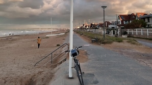 A coastal road with a bicycle parked by a white pole, leading to a beach with a few people walking.